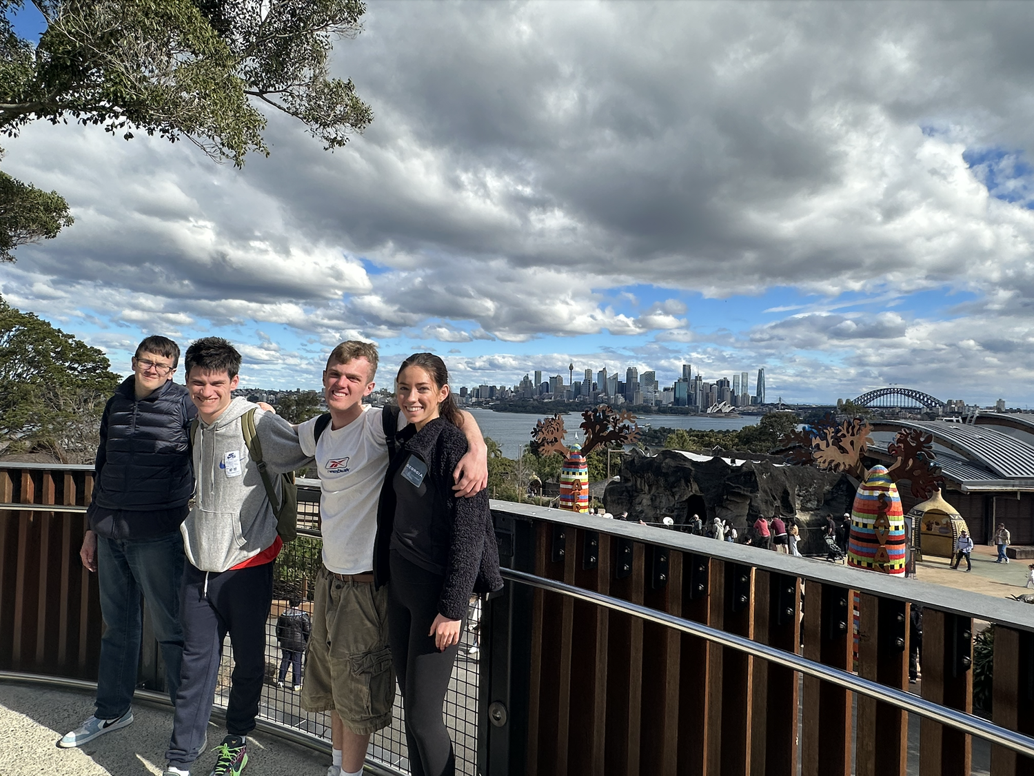 Four young adults smiling on a balcony with the Sydney skyline behind them
